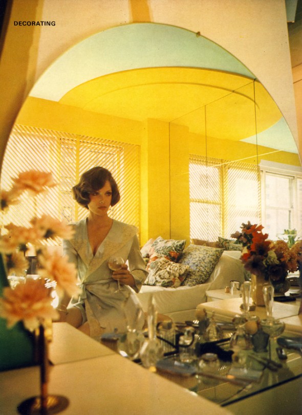 Lois Chiles relaxes with a glass of white wine, looking every inch the rising star. Bed strewn with cushions acts as extra seating, huge mirror tiles make the room look twice as large. Glass dressing table shelf laden with old scent bottles, lovingly collected over the years.
