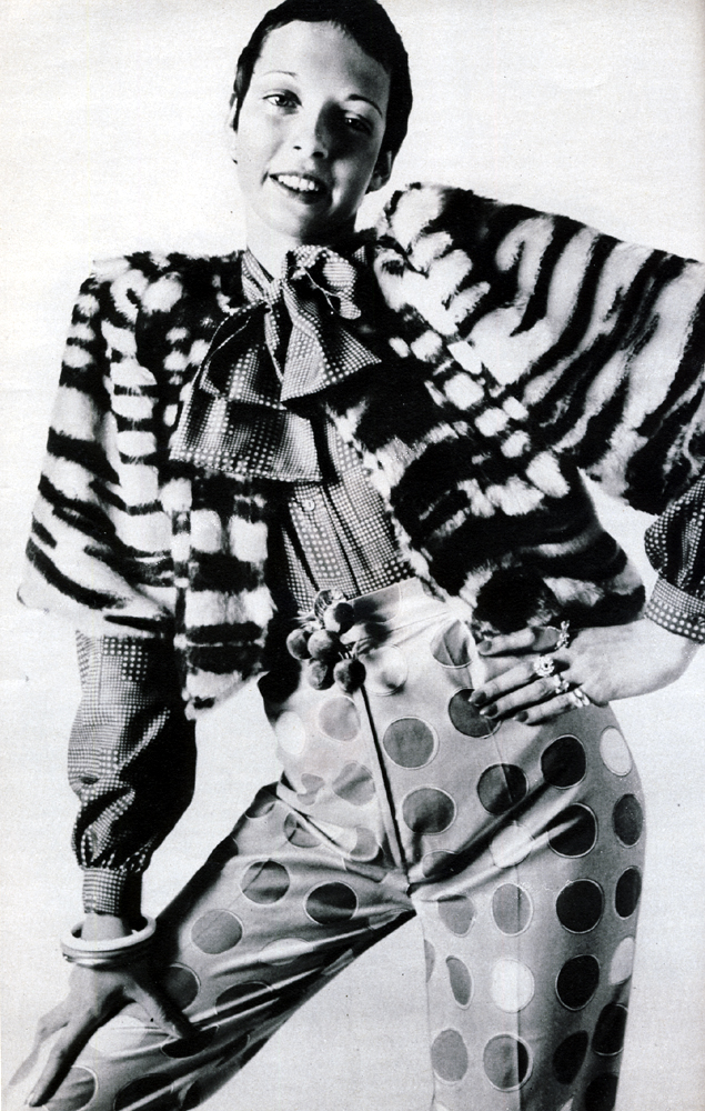 Furry tiger printed Courtelle bolero jacket and pale lemon, coffee and white coin spotted cotton satin Oxford bags, both from Martha Hill. Rust and black confetti spotted blouse by John Craig. Cherries and bangles by Adrien Mann.